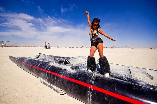 burning man - woman dancing on david best's rocket car, art car, black leg warmers, burning man art cars, dancing, furry leg warmers, long, mutant vehicles, necklaces, rocket car, topless, woman